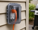 TayMac MM410CCN weatherproof in-use outlet cover installed on exterior siding with extension cord plugged into outdoor GFCI receptacle for patio and backyard use in Canada